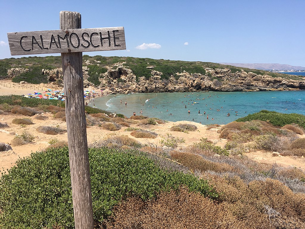 The famous crescent-shaped beach of Calamosche, a sheltered cove with light sand and transparent emerald sea.