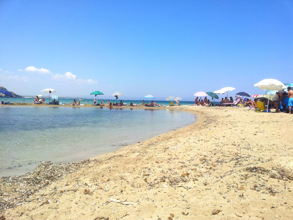 The town beach of Scalo Mandrie in Portopalo, with colorful fishing boats moored on the sand and the Island of Capo Passero in the background.